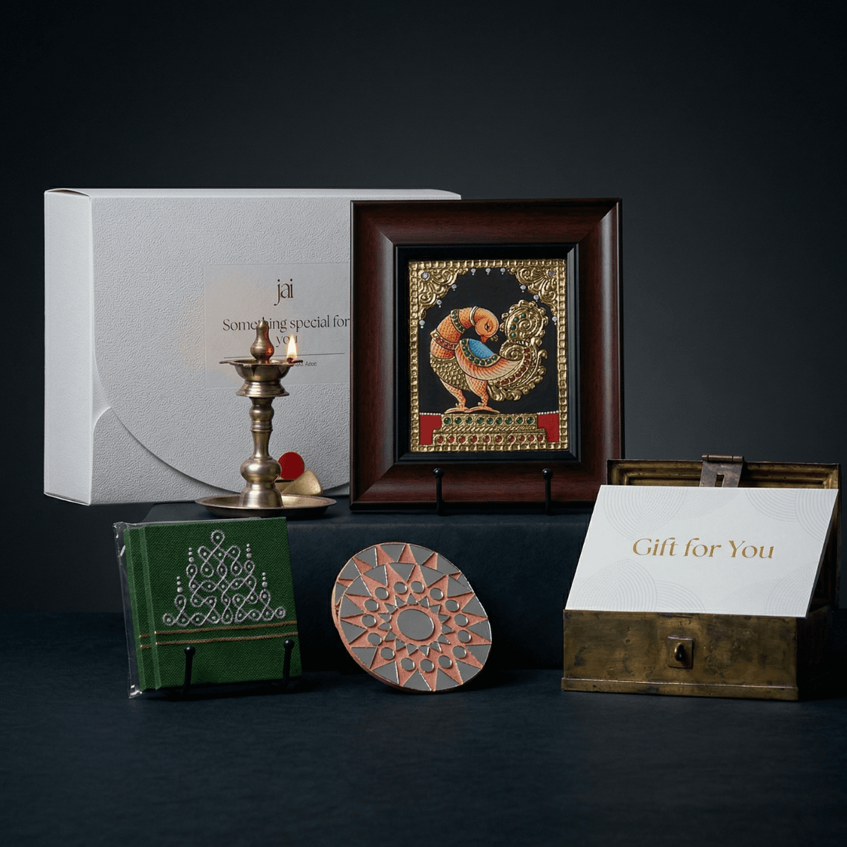 A luxury Artisan Hamper featuring a 22K gold Tanjore painting, two green hand-painted Manai, two terracotta-toned mirror mosaic coasters, and a "Gift for You" card in a premium white box.